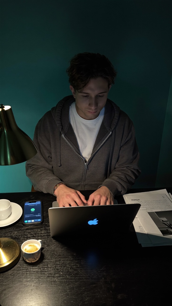 Valentino Vargas trabajando de noche en su portátil, junto a una lámpara dorada